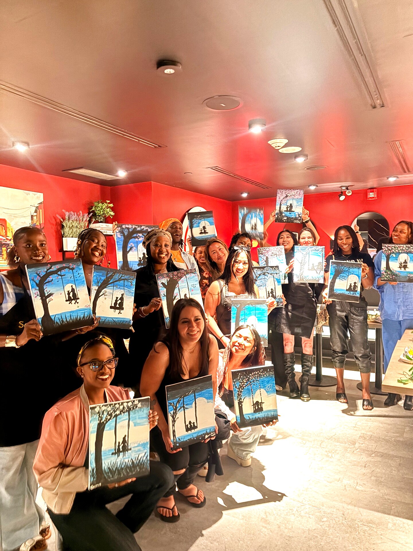 Large group of guests beaming and holding up their finished cherry blossom swing paintings