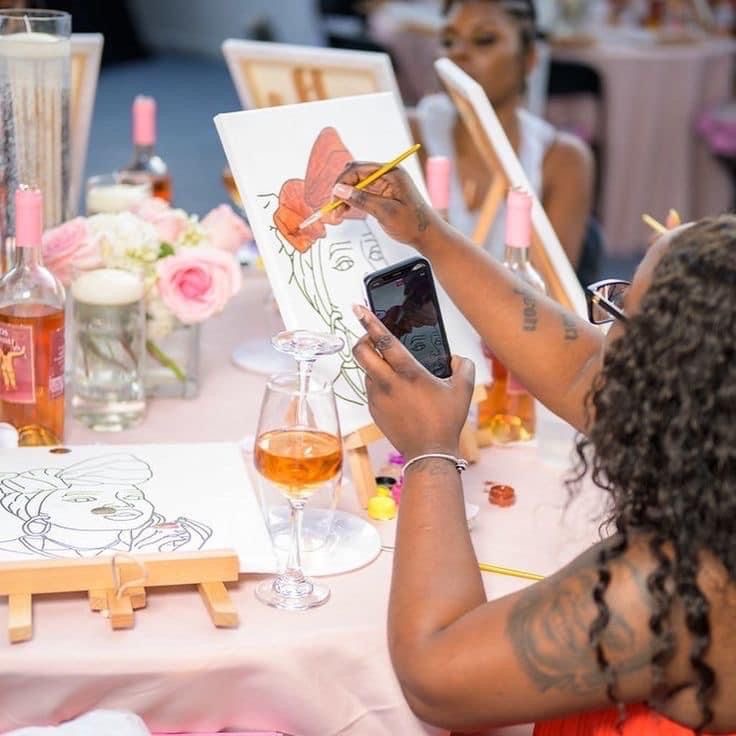 Guest painting a floral canvas surrounded by pink roses and rosé at a paint and sip night