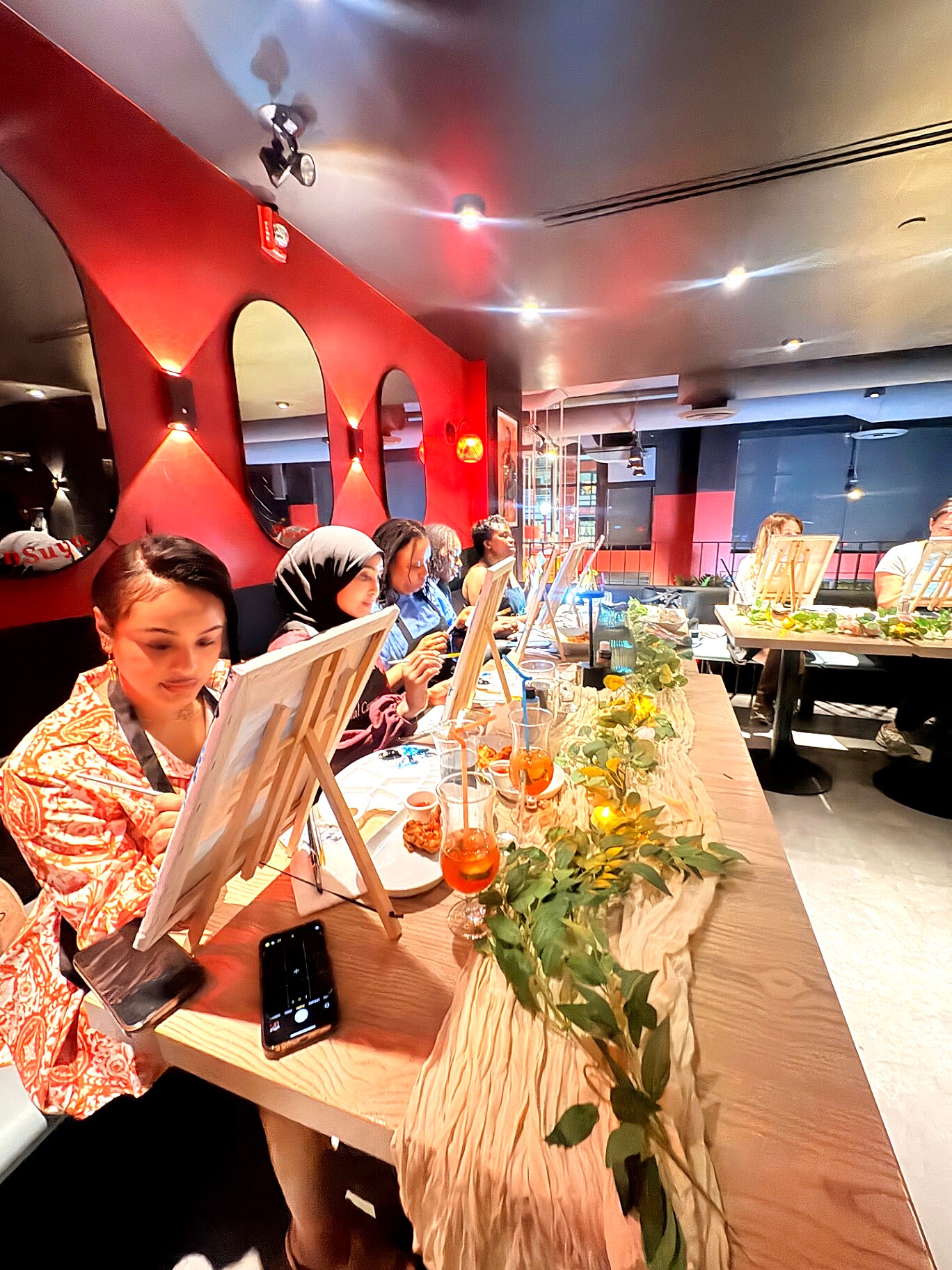 Guests painting at a long candlelit table with greenery and Aperol spritzes at VanSuya